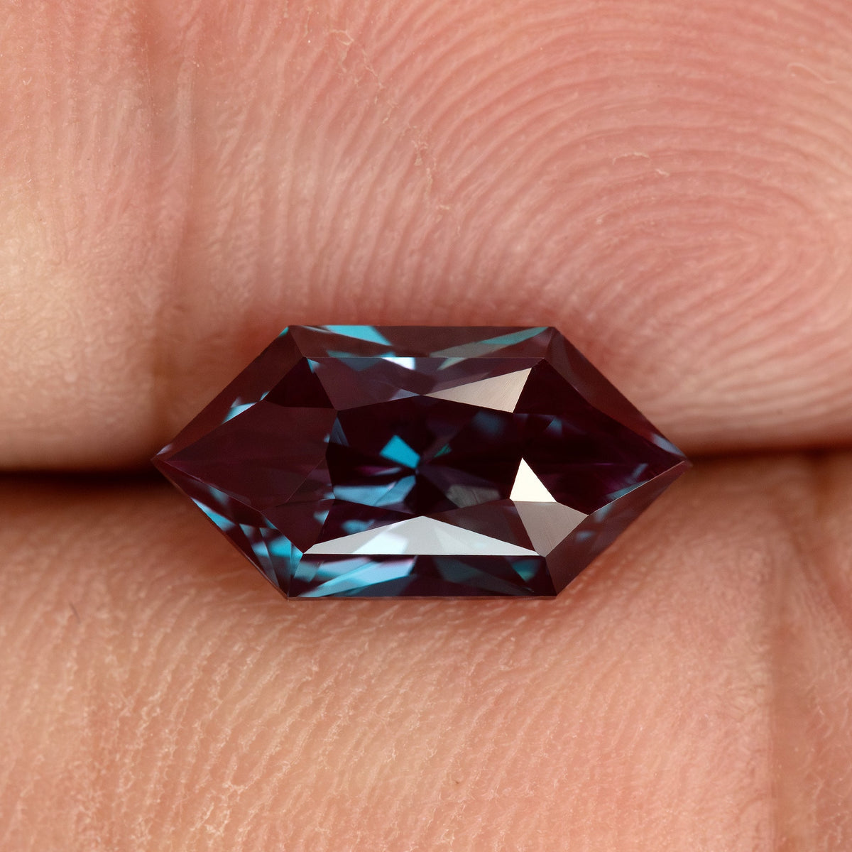 BLS112 color-change lab-grown alexandrite shown on a fingertip for an approximate sense of its 12 × 6 mm face-up size.