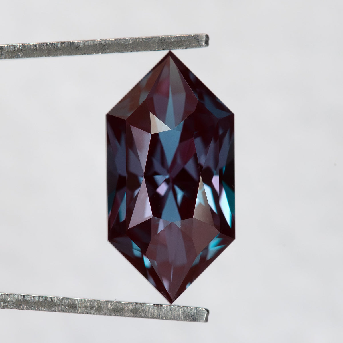 Color-change lab-grown alexandrite in tweezers, showing its pointed Dutch marquise outline and mixed facet pattern.