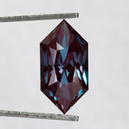 Color-change lab-grown alexandrite in tweezers, showing its pointed Dutch marquise outline and mixed facet pattern.
