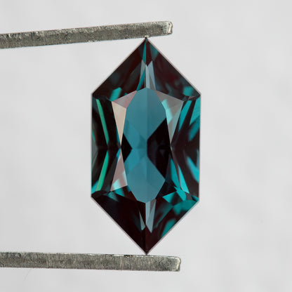 Face-up BLS113 lab-grown alexandrite in tweezers, showing its Dutch Marquise Hexagon outline and greenish blue color.
