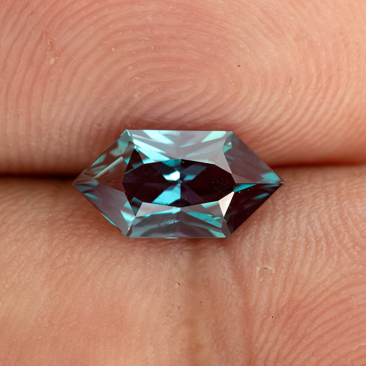 BLS113 color-change lab-grown alexandrite on a fingertip for an approximate sense of its 10 x 5 mm face-up size.
