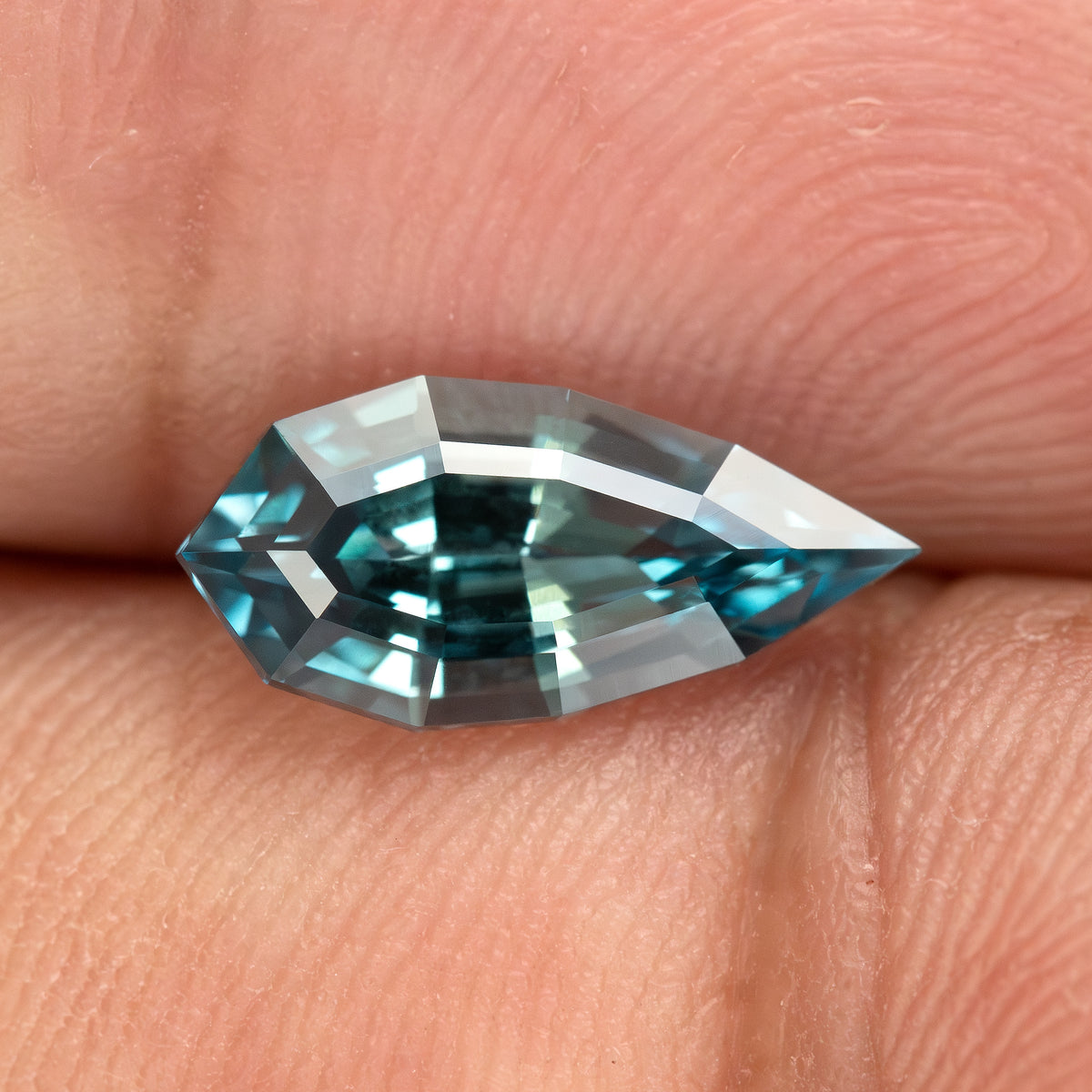 Hand-held daylight view of one BLS114 teal blue-green lab-grown sapphire.