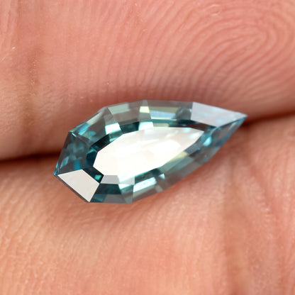 Close daylight view of one elongated pear BLS114 sapphire and its facet reflections.