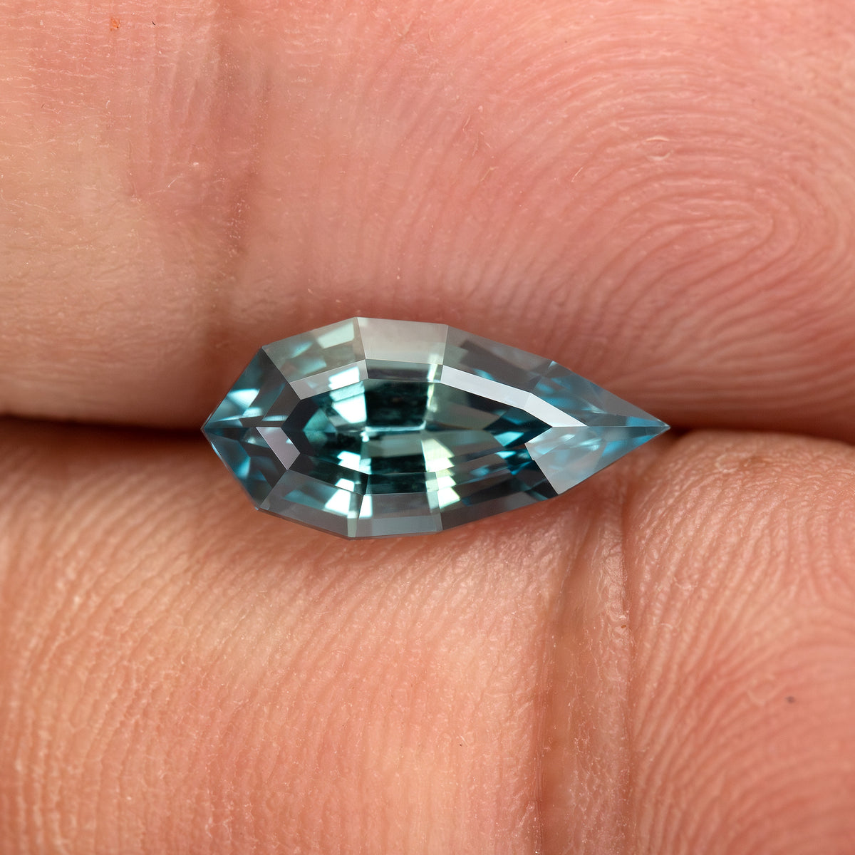 Second hand-held angle of one BLS114 teal lab-grown sapphire in daylight.