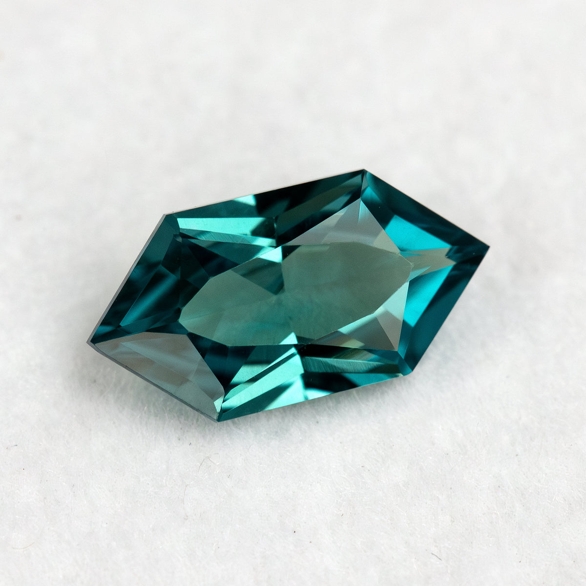 Alternate angle of BLS115 teal green lab-grown sapphire, showing blue-green reflections across the facet pattern.