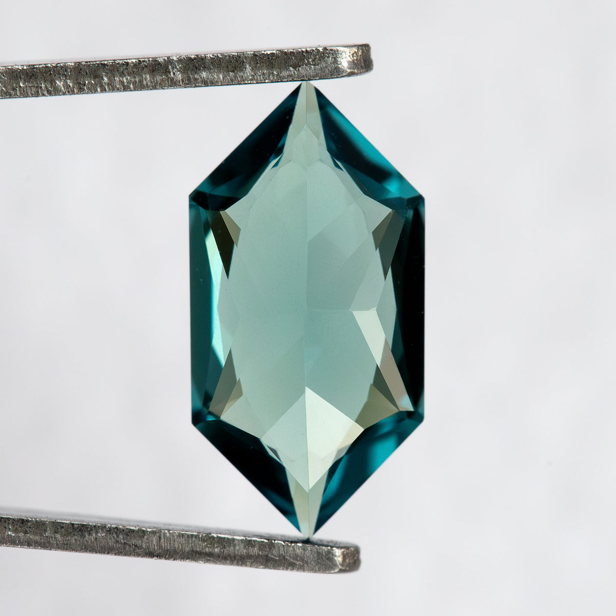 Pavilion and back view of BLS115 lab-grown sapphire in tweezers, showing the elongated geometric cut.