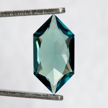 Pavilion and back view of BLS115 lab-grown sapphire in tweezers, showing the elongated geometric cut.