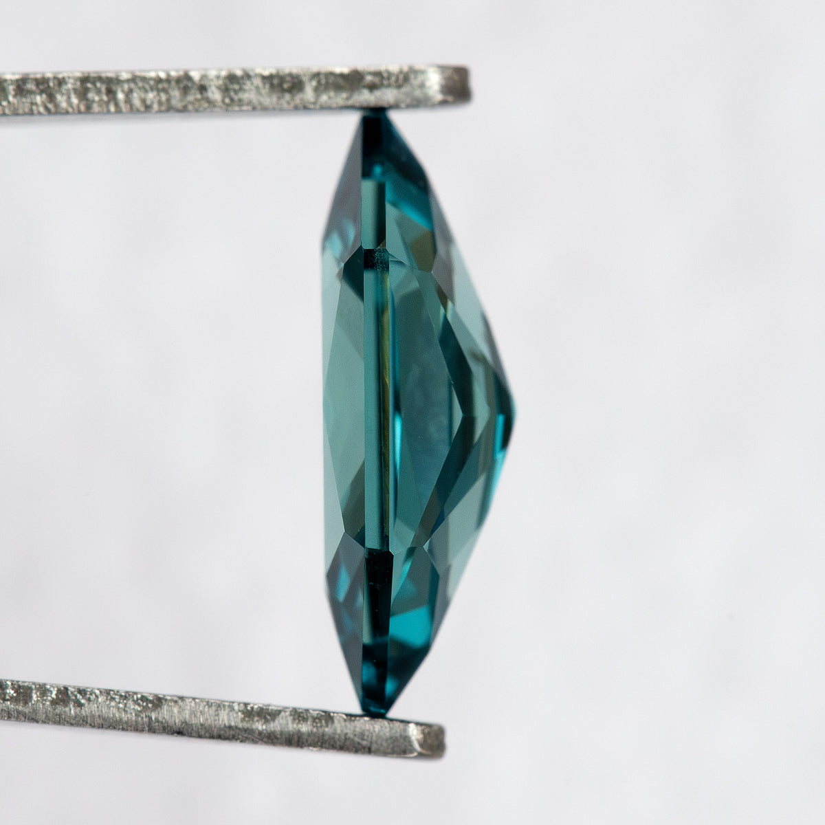 Side profile of BLS115 lab-grown sapphire in tweezers, showing its crown, girdle and pavilion depth.