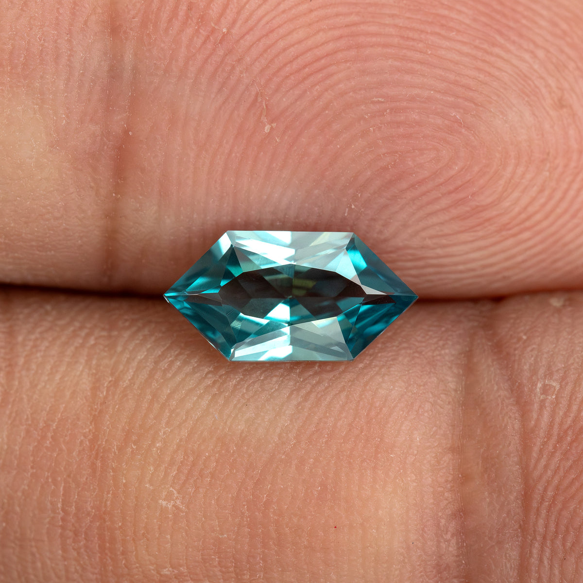 BLS115 teal green lab-grown sapphire on a fingertip for an approximate sense of its 10 x 5 mm face-up size.