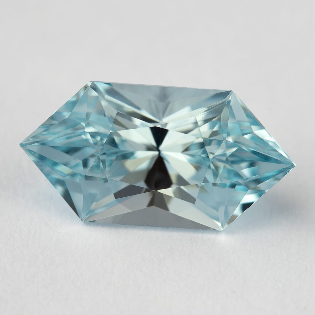Horizontal face-up view of an aquamarine-blue lab-grown sapphire, showing its pointed ends and alternating light and dark facets.