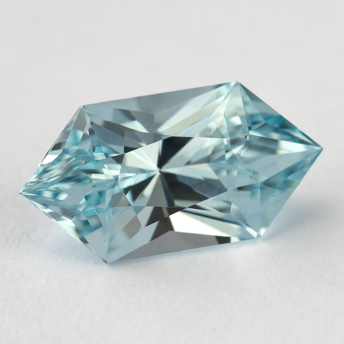 Angled face-up view of the pale-blue lab-grown sapphire, showing reflections across its elongated hexagon outline.