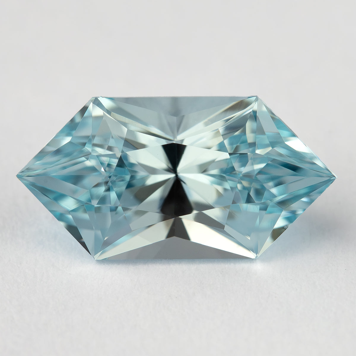 Aquamarine-blue lab-grown sapphire viewed face-up on a pale surface, with bright triangular facet reflections.