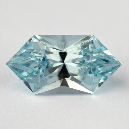 Aquamarine-blue lab-grown sapphire viewed face-up on a pale surface, with bright triangular facet reflections.