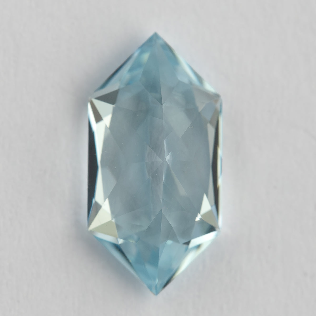Vertical view of the elongated hexagon lab-grown sapphire on a pale background, showing its pointed ends.