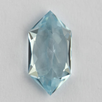 Vertical view of the elongated hexagon lab-grown sapphire on a pale background, showing its pointed ends.