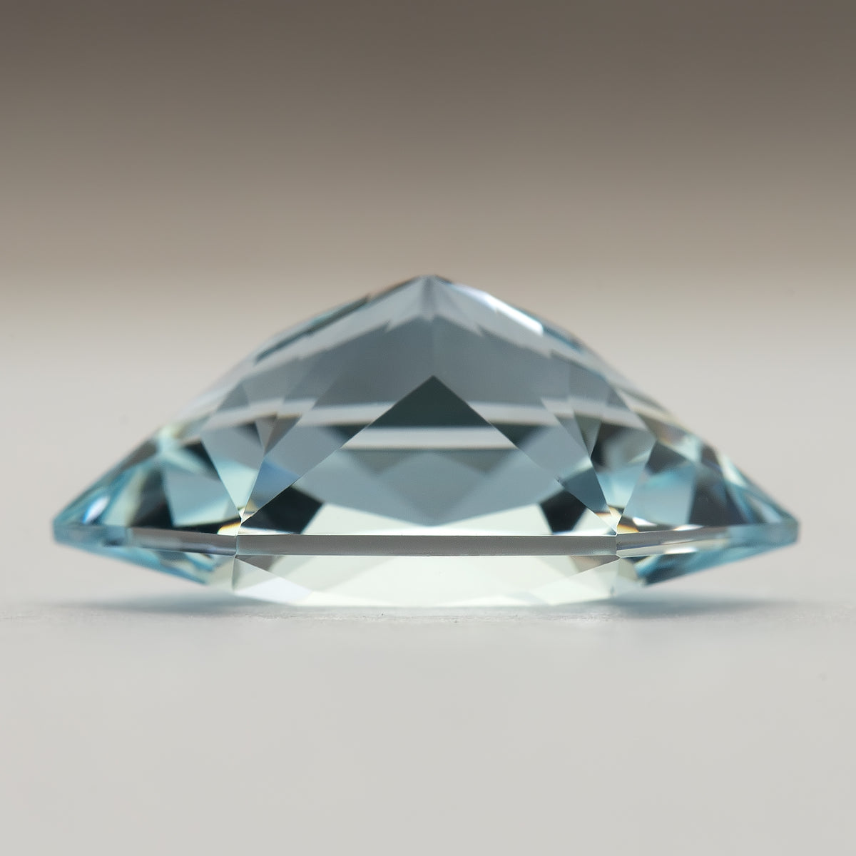 Side profile of the lab-grown sapphire on a pale surface, showing its crown and pavilion silhouette.