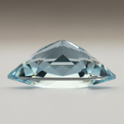 Side profile of the lab-grown sapphire on a pale surface, showing its crown and pavilion silhouette.