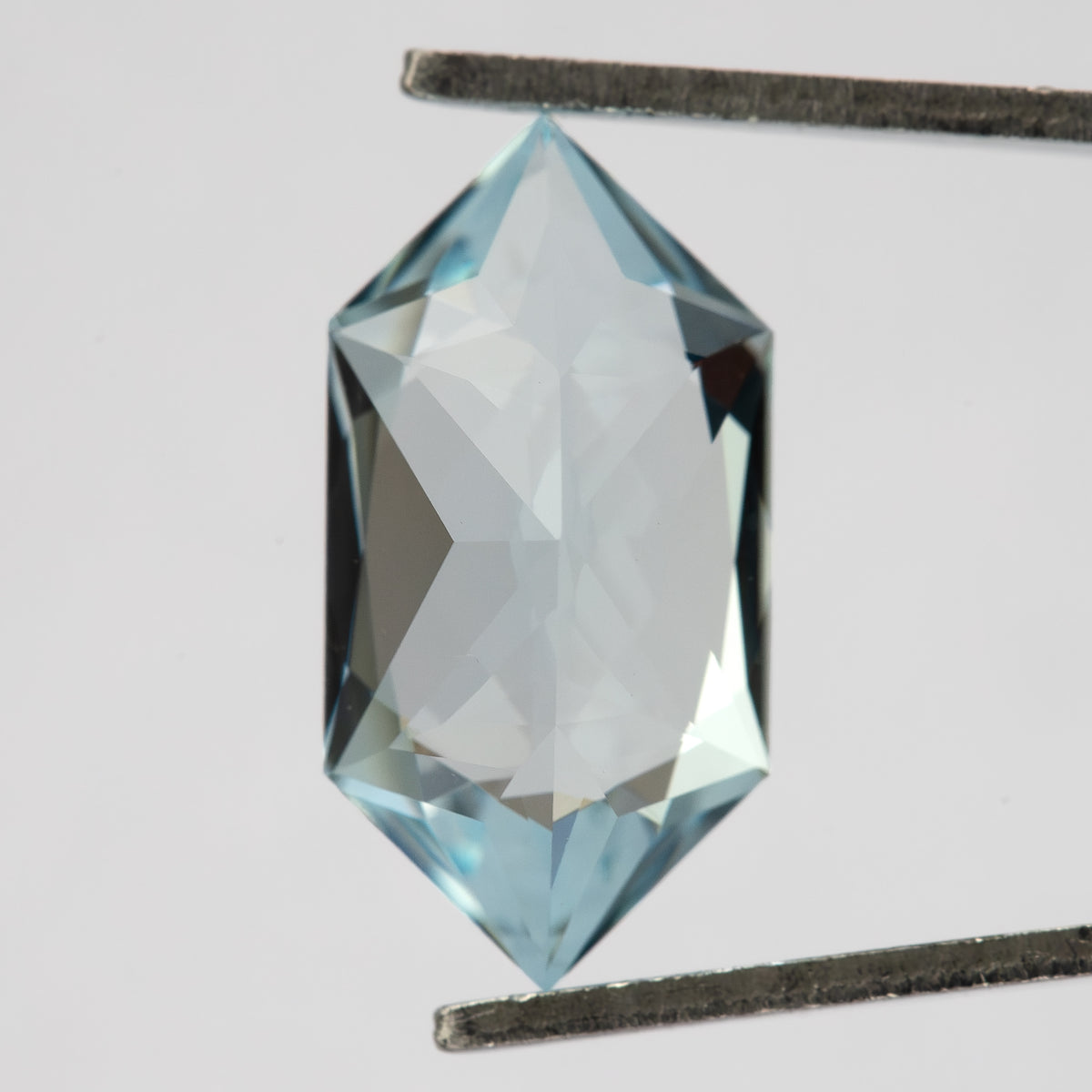 Reverse view of the pale-blue lab-grown sapphire held vertically in tweezers, showing broad pavilion facets.