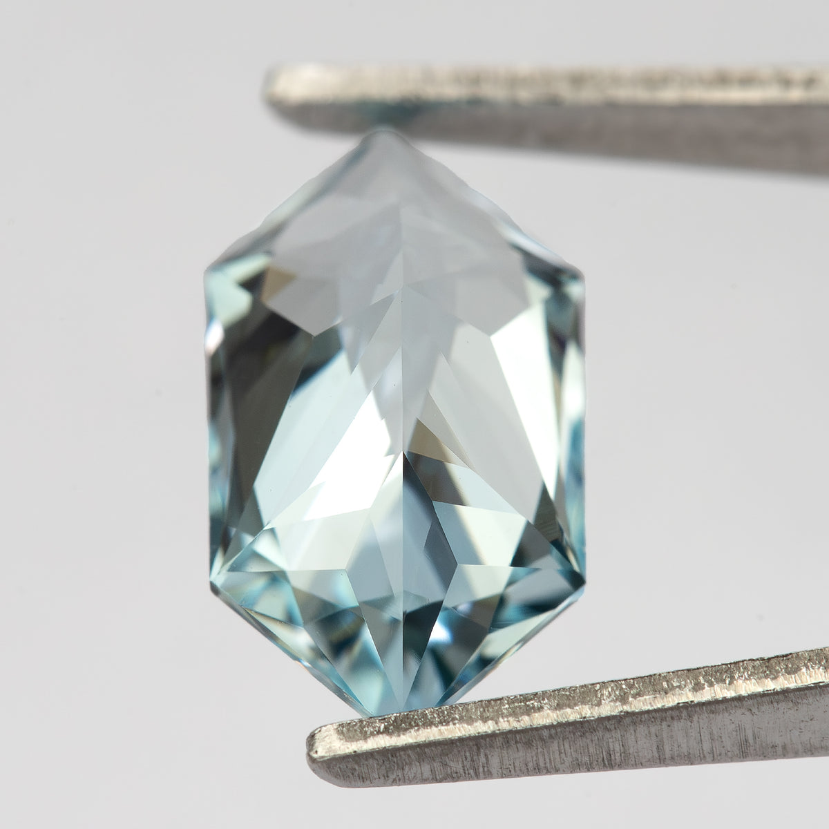 Angled reverse view of the lab-grown sapphire in tweezers, showing pale-blue reflections across the pavilion.