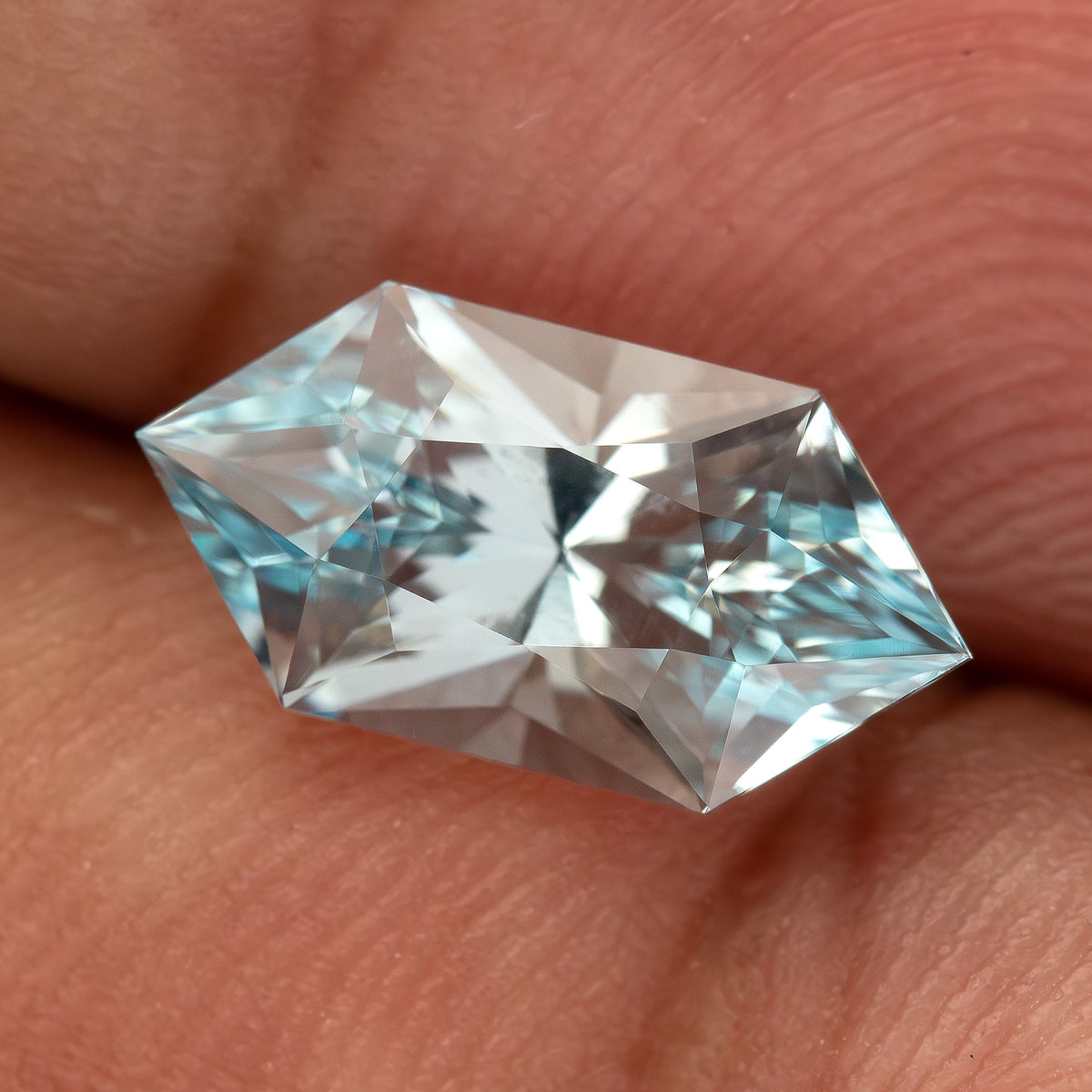Aquamarine-blue lab-grown sapphire resting horizontally on a fingertip, showing its face-up facet pattern.