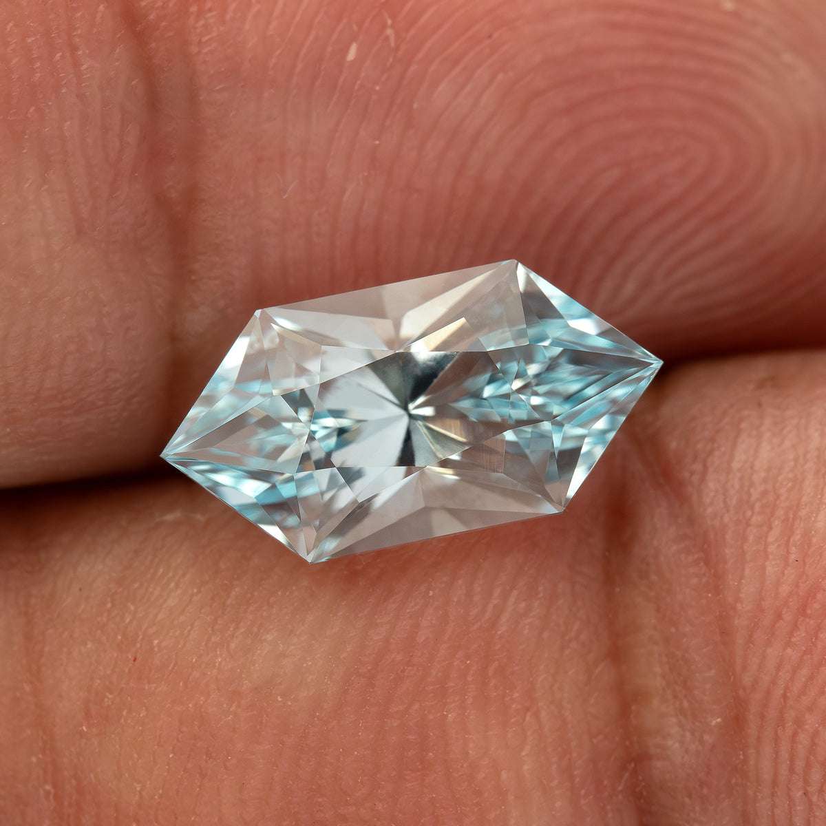 Angled face-up view of the lab-grown sapphire resting on a fingertip against a warm skin background.