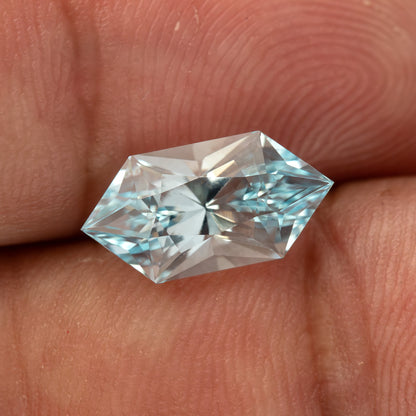 Angled face-up view of the lab-grown sapphire resting on a fingertip against a warm skin background.