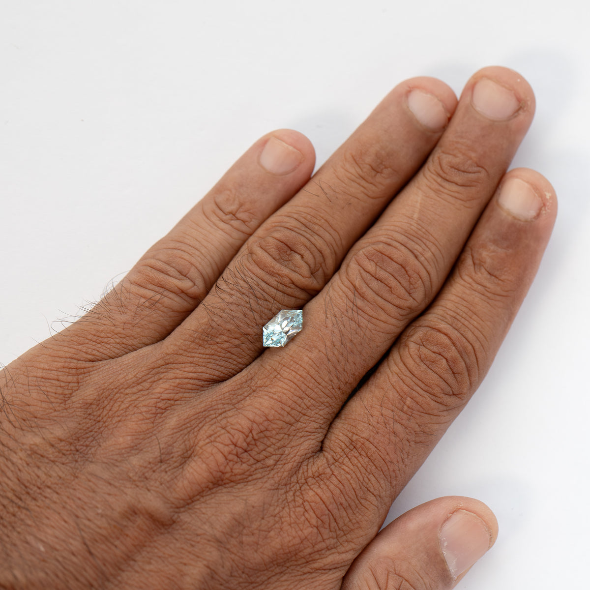 The loose pale-blue sapphire resting on the back of a hand, providing a visual size reference.