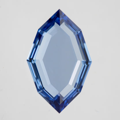 Blue portrait-cut lab-grown sapphire viewed face-up vertically on white, with a broad transparent table and stepped hexagonal outline.
