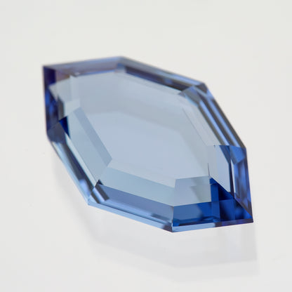 Blue portrait-cut sapphire tilted on white, showing the broad pale table and blue edge facets.