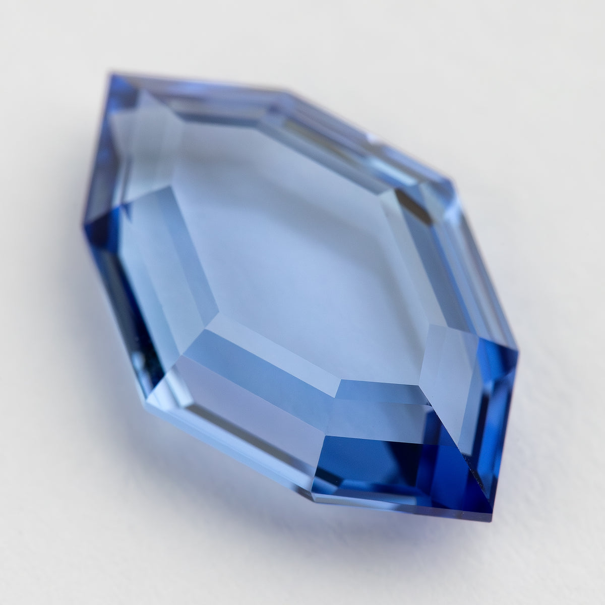 Angled face-up view of the blue portrait-cut sapphire with pale central reflections and darker blue points.