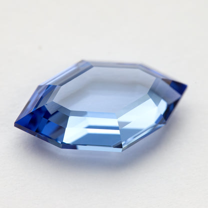 Blue portrait-cut sapphire at a low face-up angle, with a broad light reflection across the shallow centre.