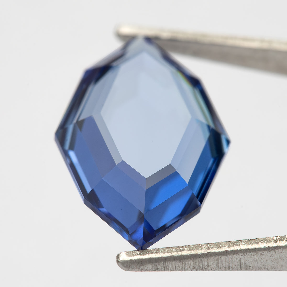 Pavilion-side view of the blue portrait-cut sapphire held vertically in tweezers.