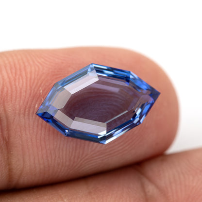 Tilted view of the blue portrait-cut sapphire on fingertips, showing its shallow step-cut edges.