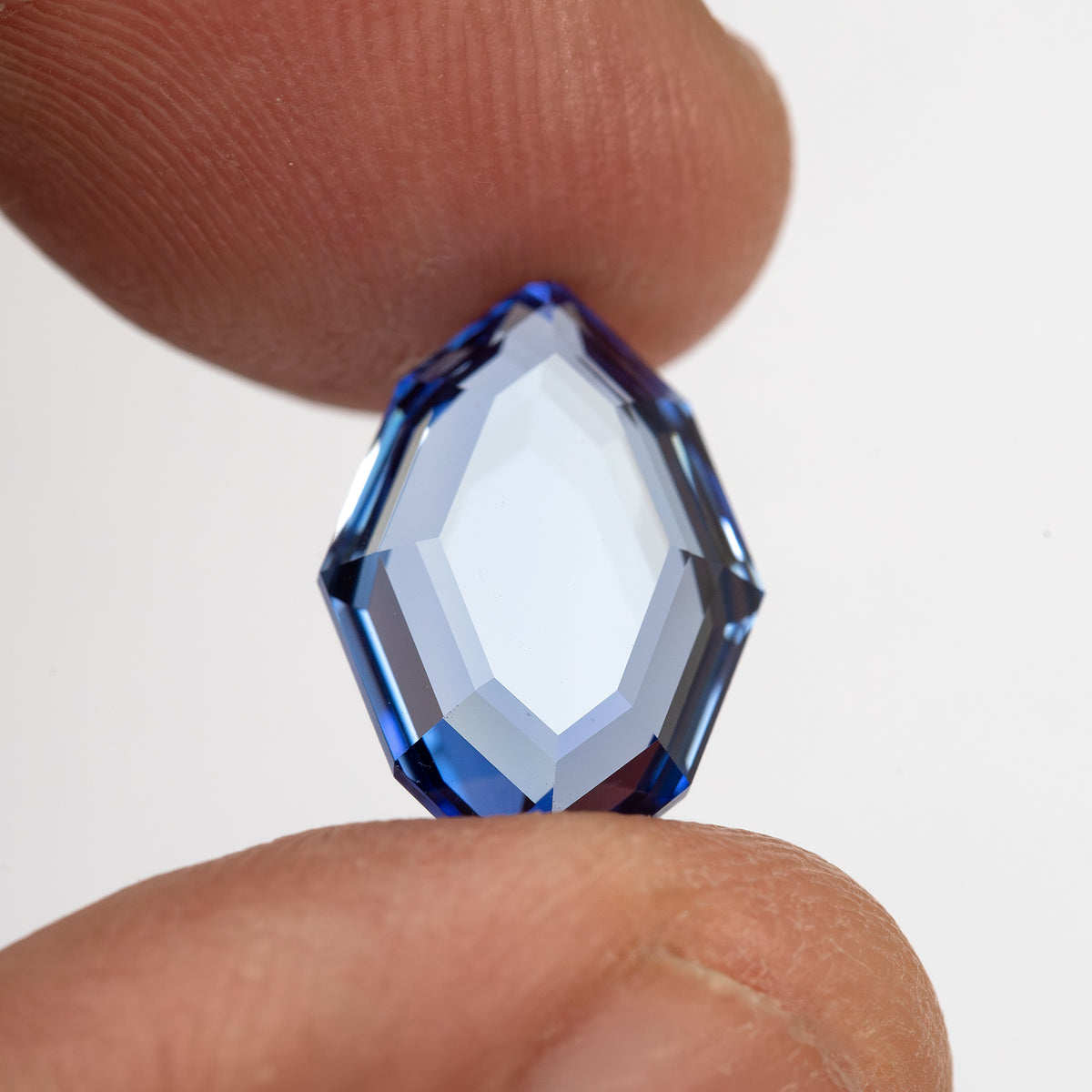 Blue portrait-cut sapphire held upright face-up between fingertips for scale.