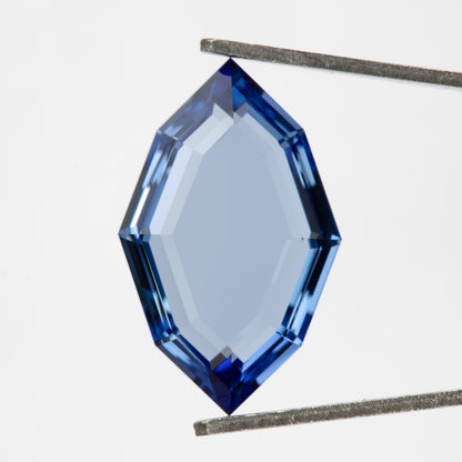Blue portrait-cut sapphire held face-up in tweezers, with white visible through its large central table.