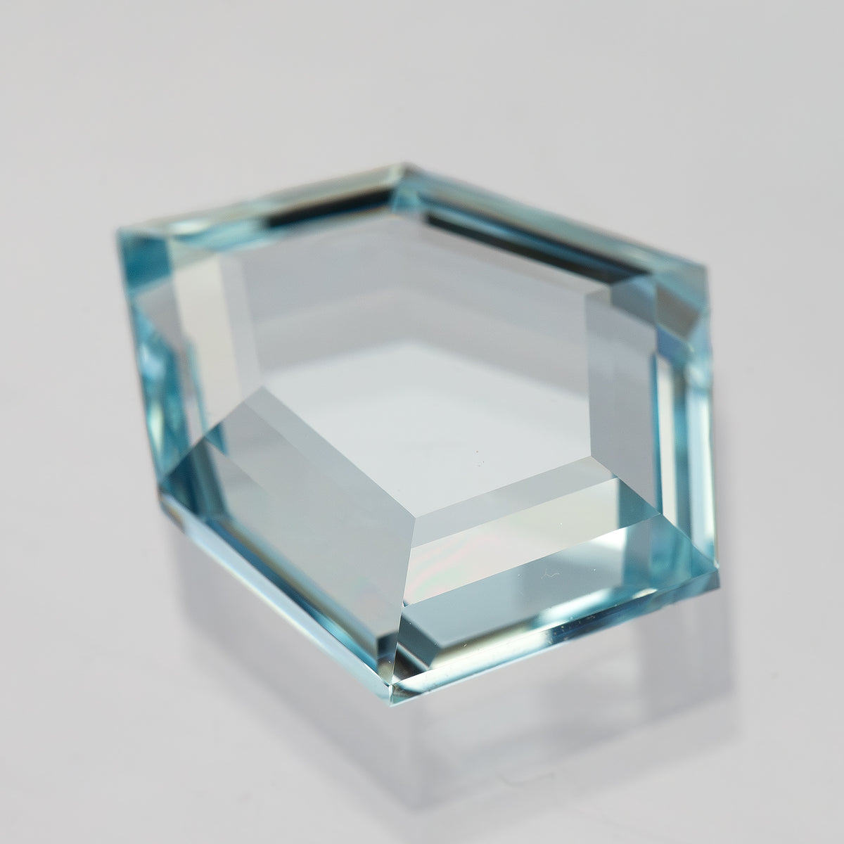 Aquamarine-blue shield-shaped lab-grown sapphire tilted face-up, showing changing light reflections. View 8.