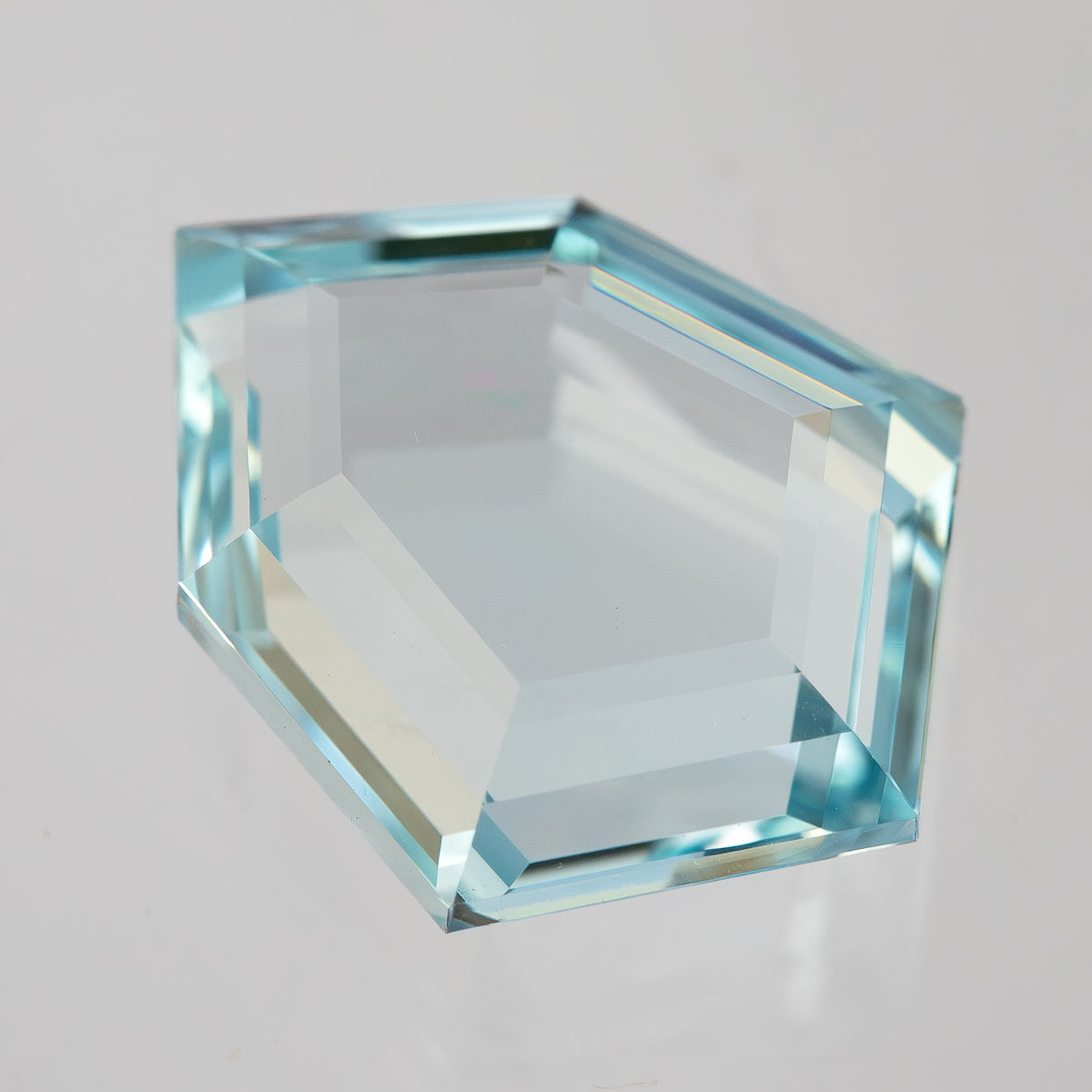 Aquamarine-blue shield-shaped lab-grown sapphire tilted face-up, showing changing light reflections. View 9.