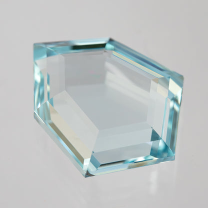 Aquamarine-blue shield-shaped lab-grown sapphire tilted face-up, showing changing light reflections. View 9.