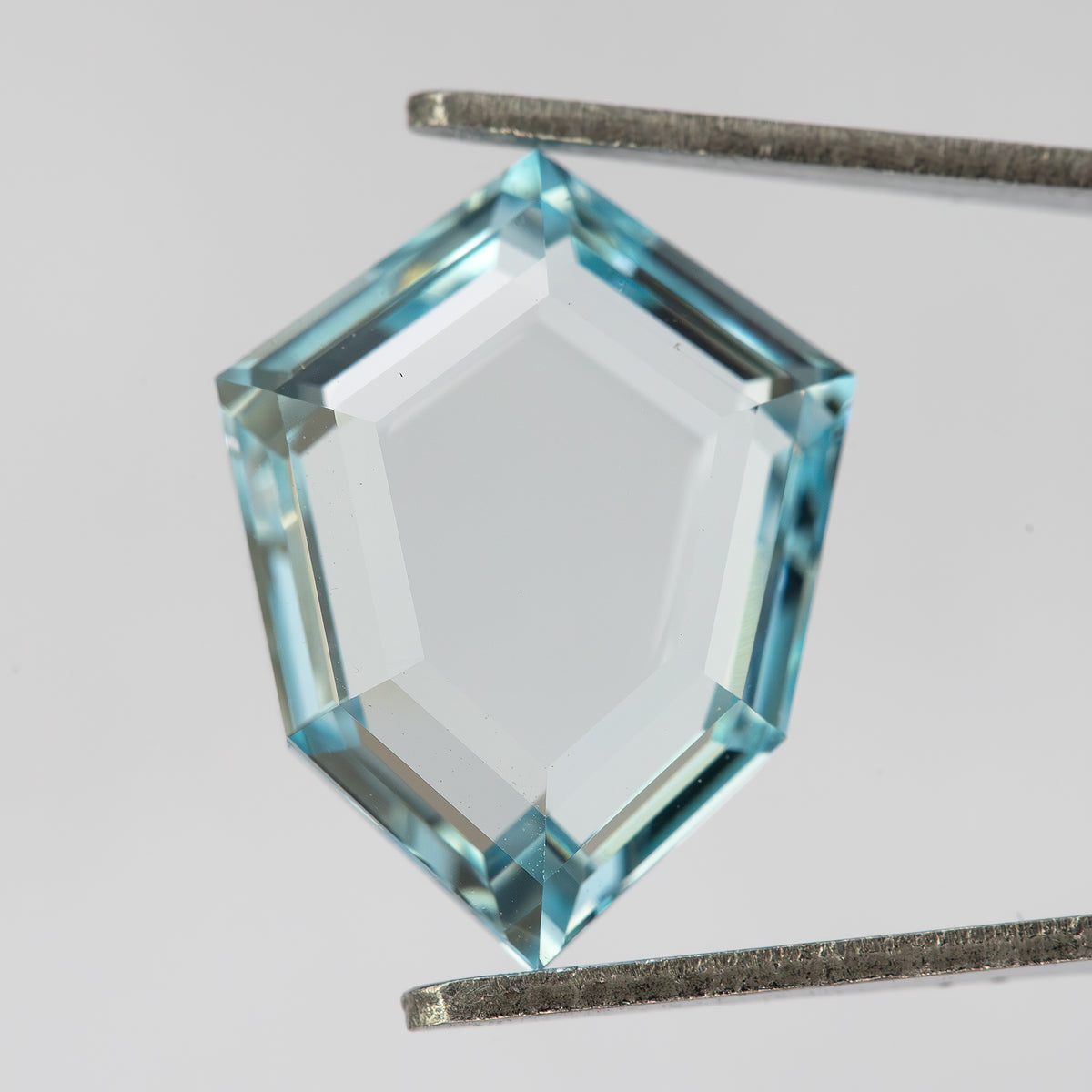 Aquamarine-blue shield-shaped lab-grown sapphire shown at an angle from the pavilion side. View 12.