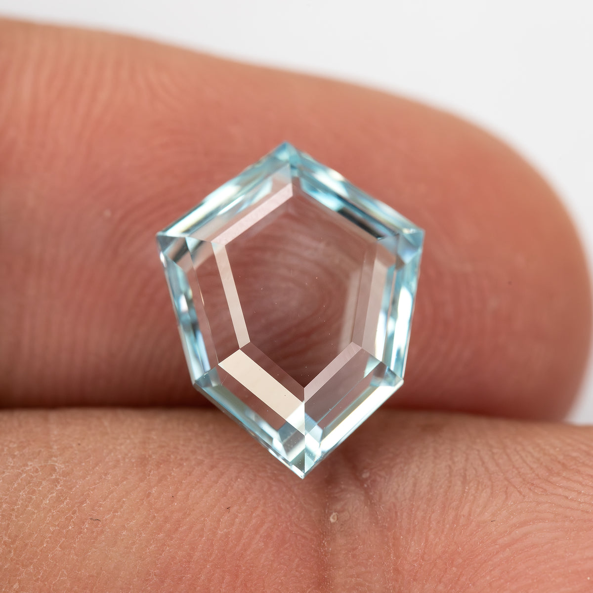Aquamarine-blue shield-shaped lab-grown sapphire resting on fingertips for scale. View 4.