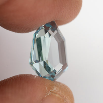 Aquamarine-blue shield-shaped lab-grown sapphire viewed from the side, showing crown and pavilion depth. View 14.