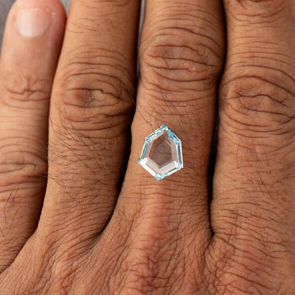 Aquamarine-blue shield-shaped lab-grown sapphire shown against a hand for scale. View 5.