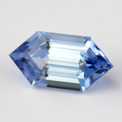Blue elongated-hexagon lab-grown sapphire on white, with bright broad reflections across the step facets.