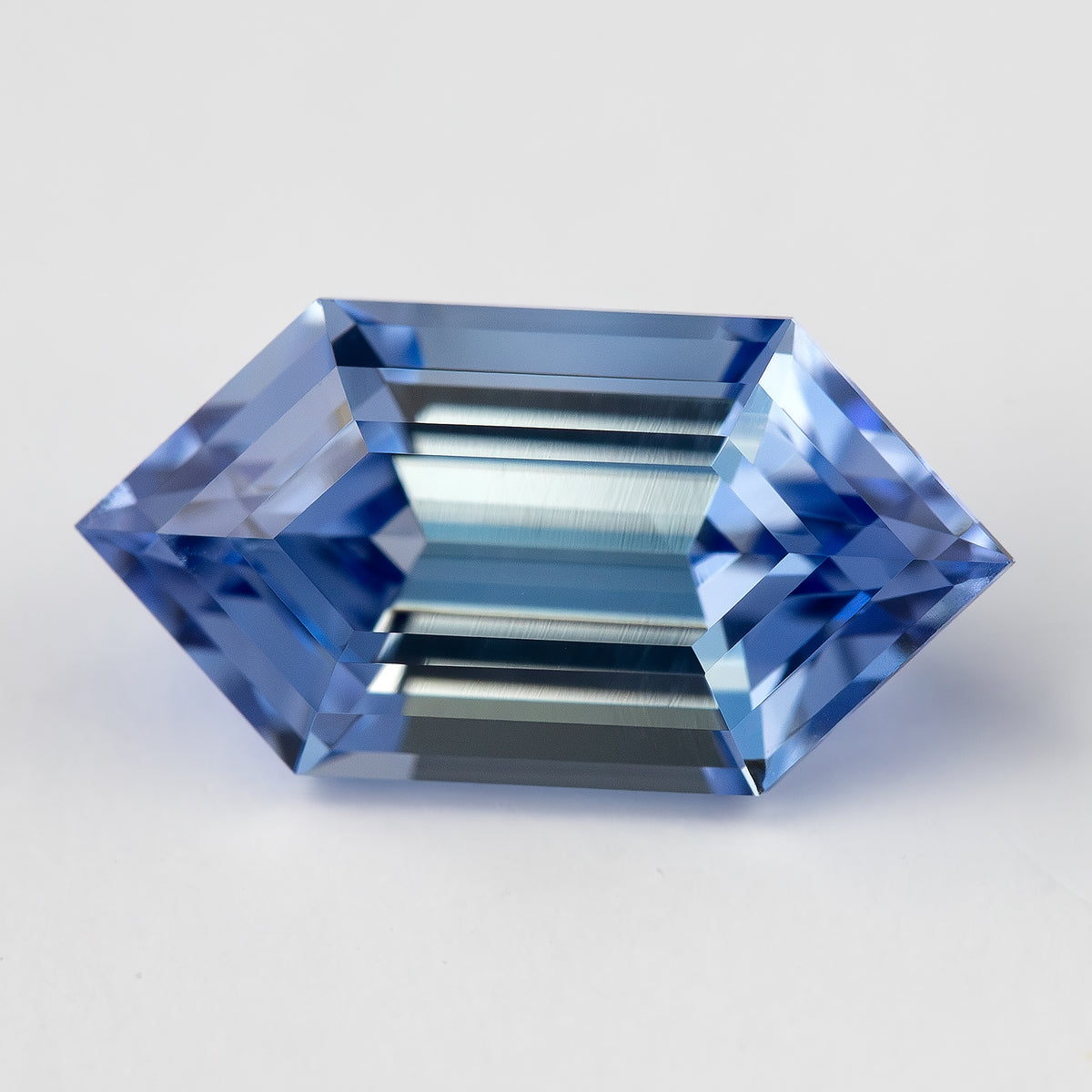 Face-up view of a blue lab-grown sapphire with a long hexagon outline and clearly defined step-cut reflections.