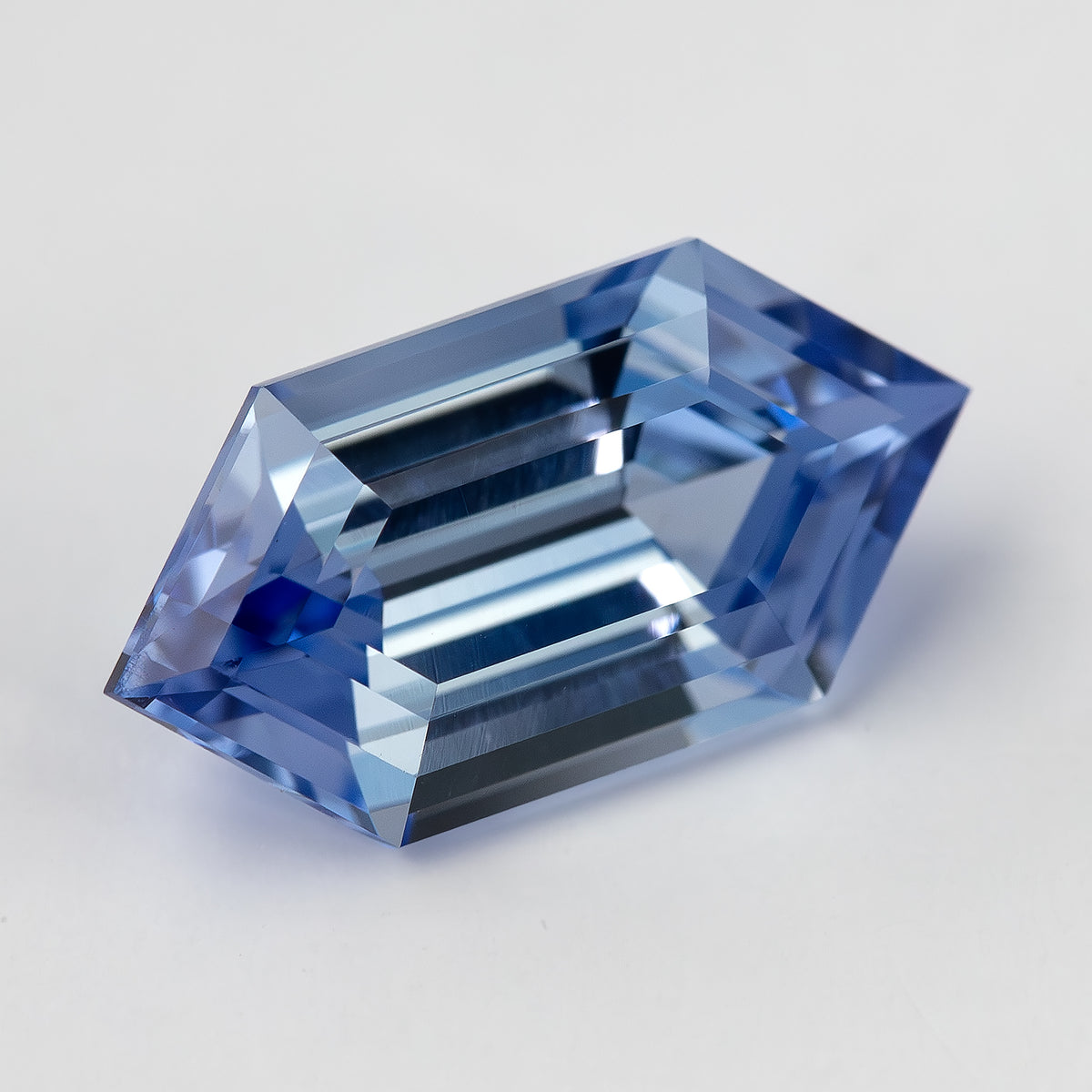 Blue long-hexagon lab-grown sapphire at an angle, showing its outline, broad table and surrounding step facets.