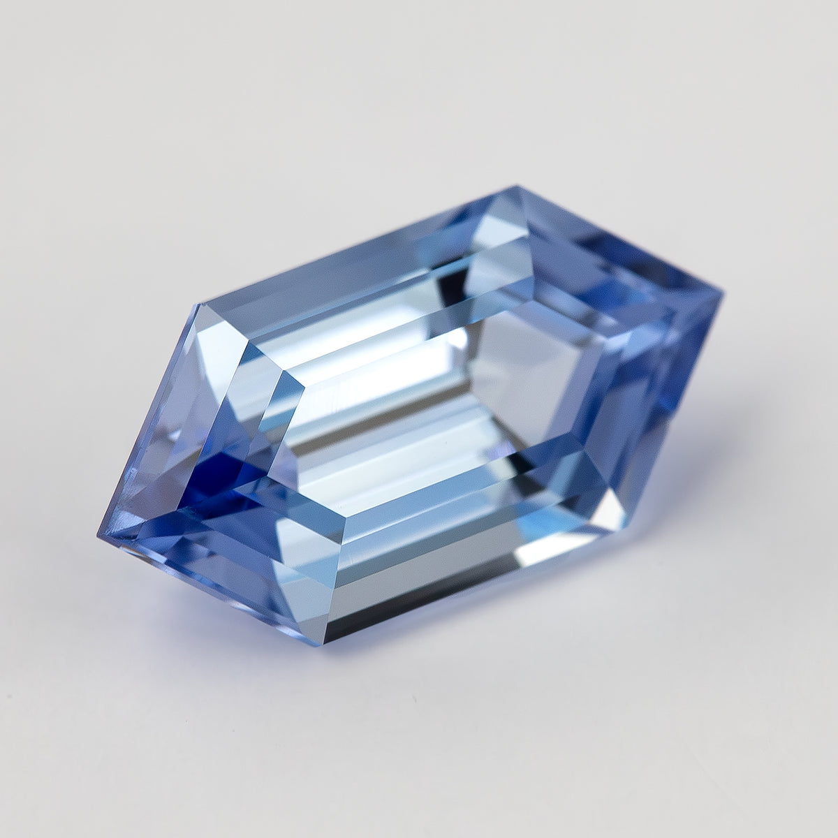 The blue step-cut lab-grown sapphire tilted diagonally on white, with its pointed ends fully visible.