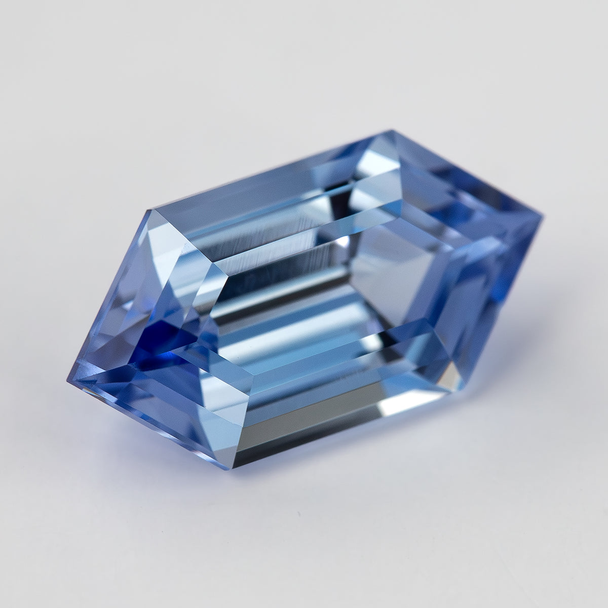 Closer angled view of the blue long-hexagon lab-grown sapphire, showing alternating pale and dark step reflections.