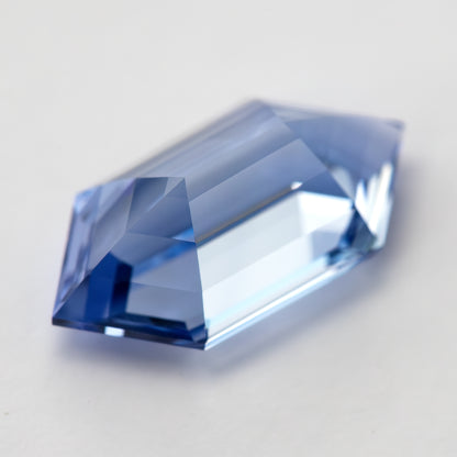 The blue long-hexagon sapphire from a low oblique angle, showing its height and step-faceted side.