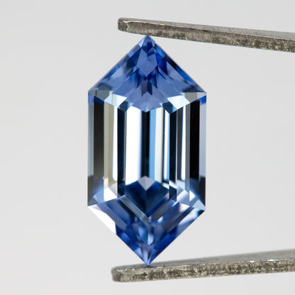 Blue lab-grown sapphire held upright in tweezers, showing the complete long-hexagon outline and step-cut face.