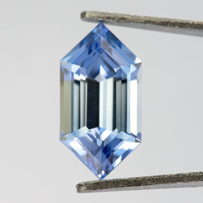 Blue step-cut sapphire in tweezers at a slight angle, showing pale central reflections and blue pointed ends.